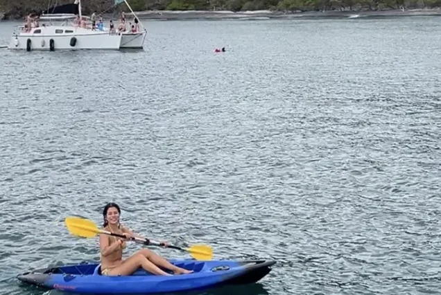 A traveler paddling a kayak with a catamaran sailboat along the pacific coast of Guanacaste, Costa Rica